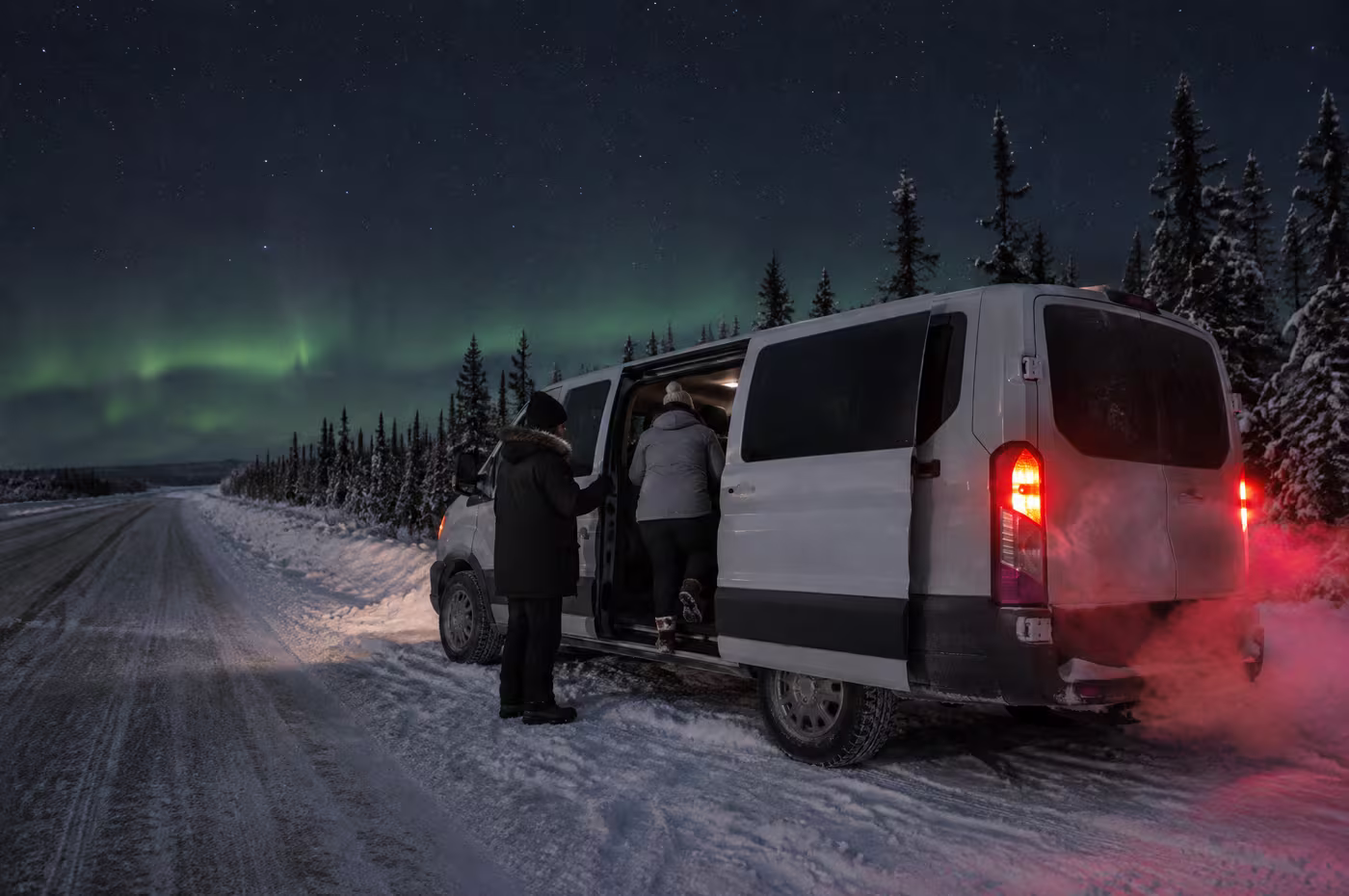 A guide holding the van door open for a guest on a snowy highway shoulder at night