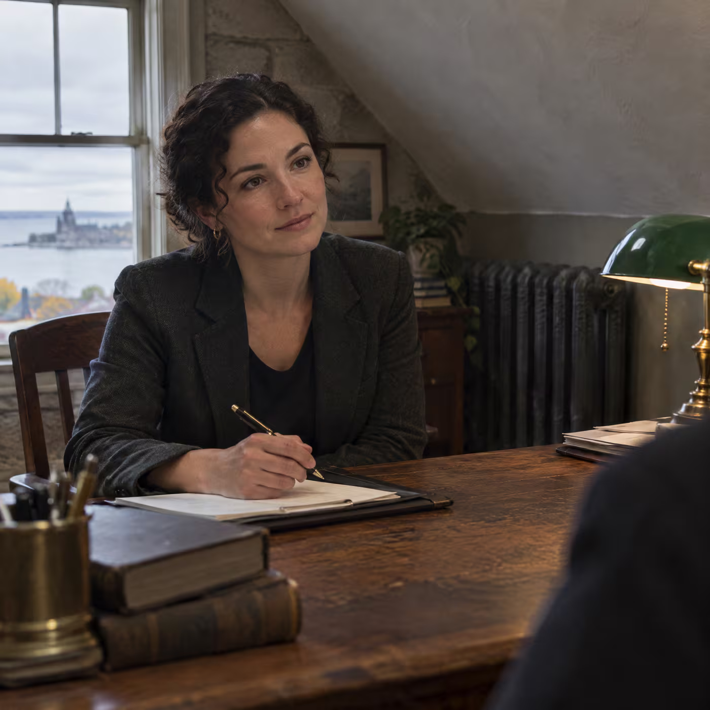 Anneke Brouwer at an oak desk under a green desk lamp, pen in hand
