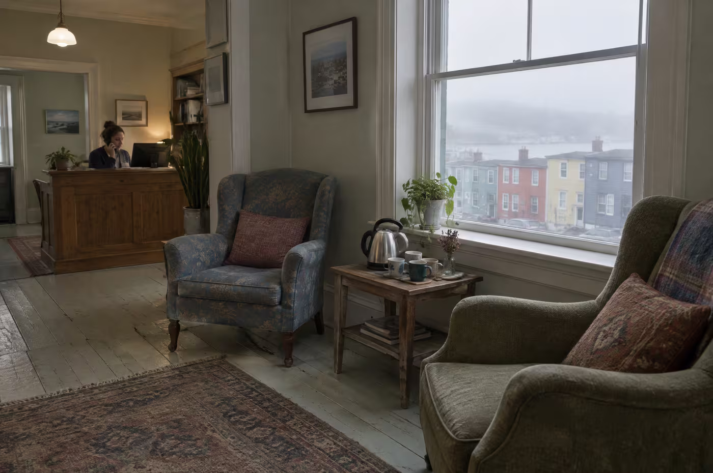 A small waiting room with armchairs, a kettle and a sash window onto fog and coloured row houses