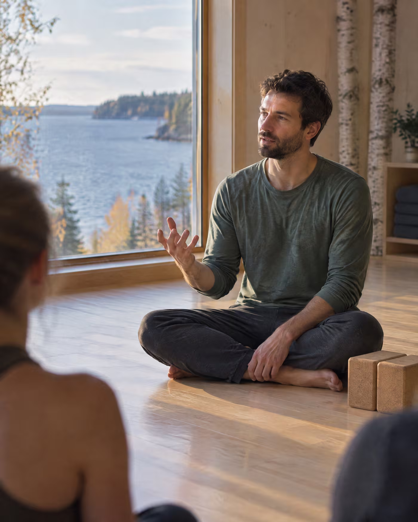 Owen, a bearded teacher sitting cross-legged and explaining a pose to the class