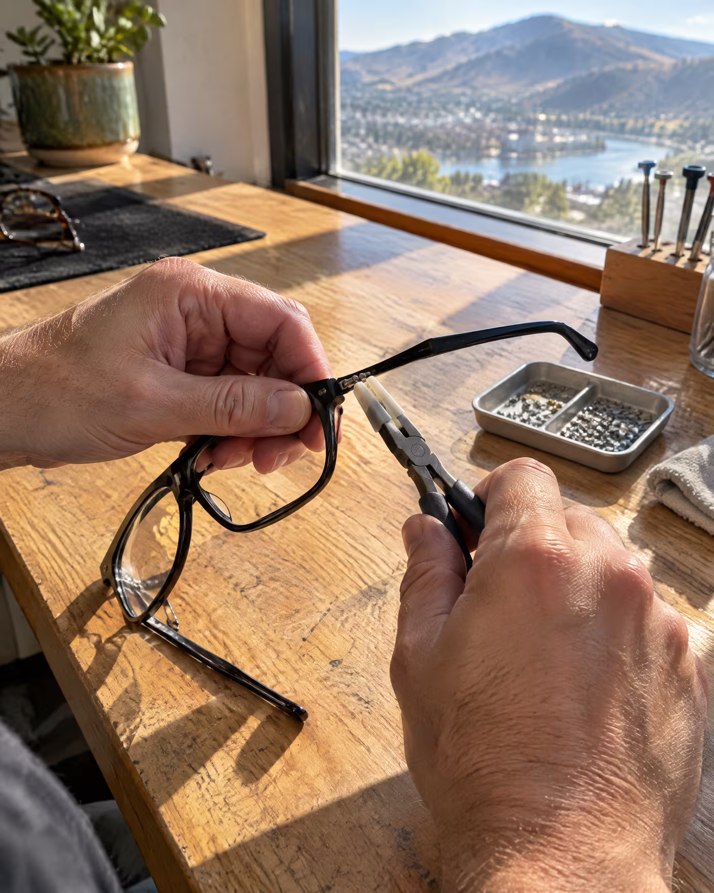 An optician's hands adjusting the arm of black acetate glasses with nylon pliers