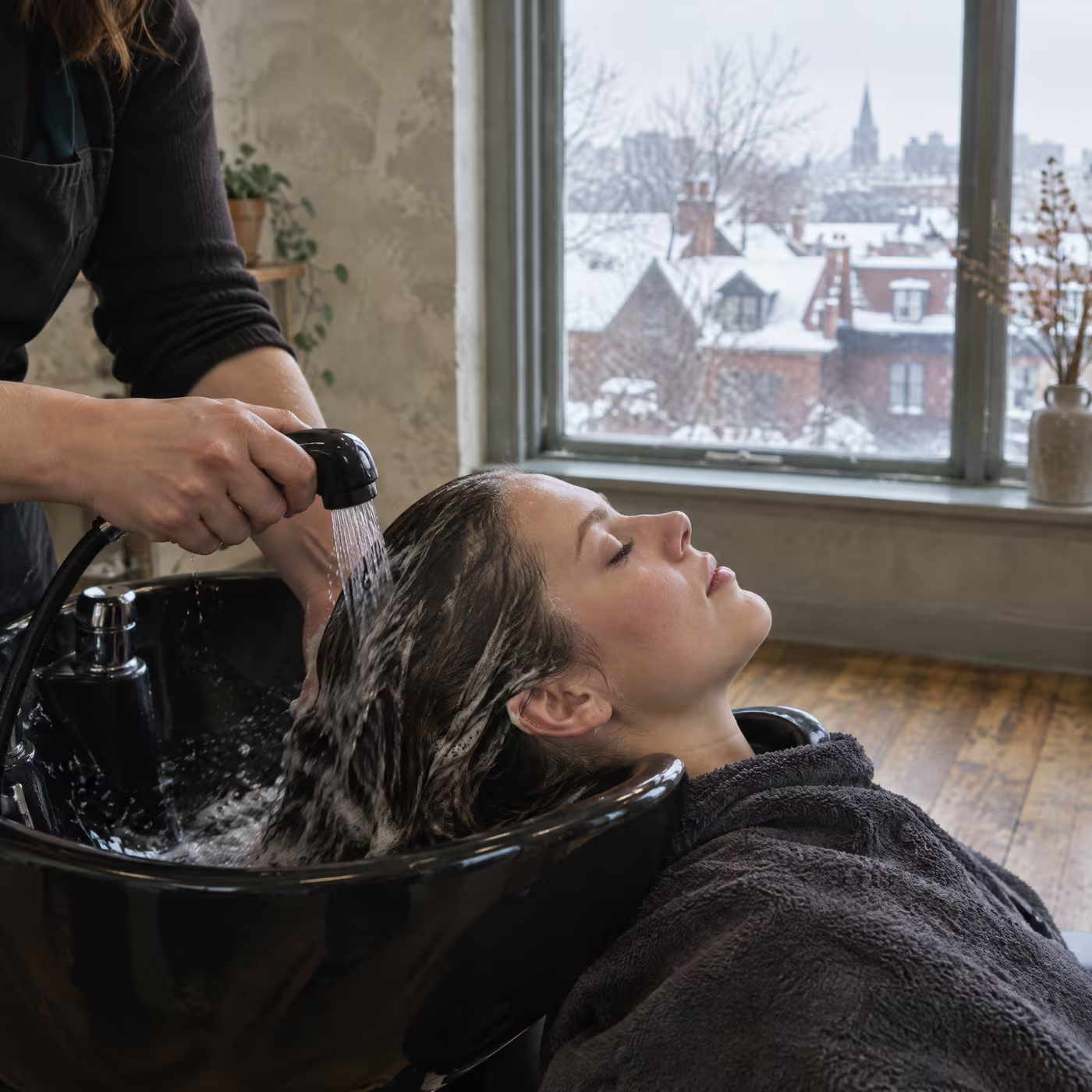 A stylist rinsing lather from a client's hair at a black basin