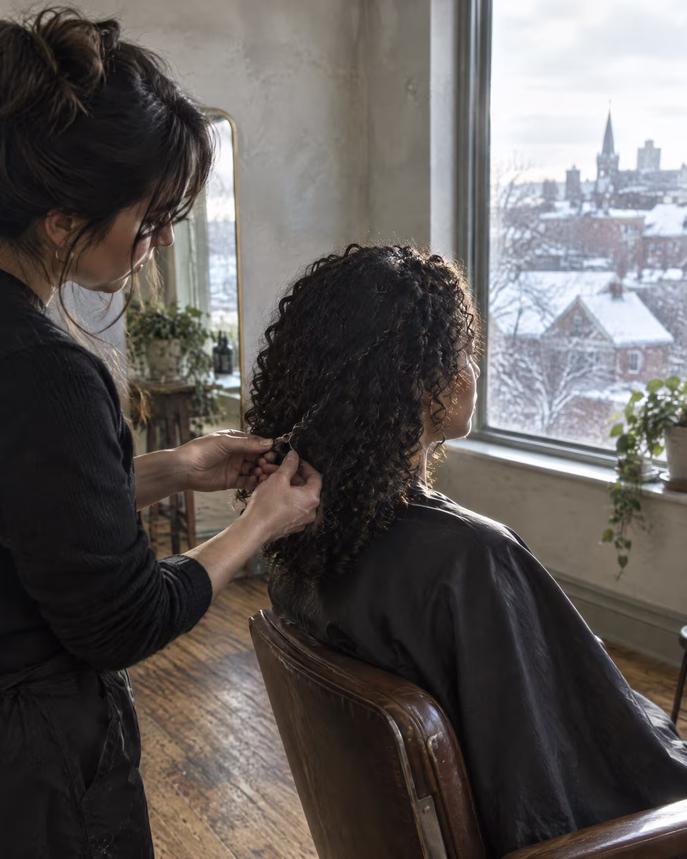 A stylist defining the ends of a client's curls against the window light