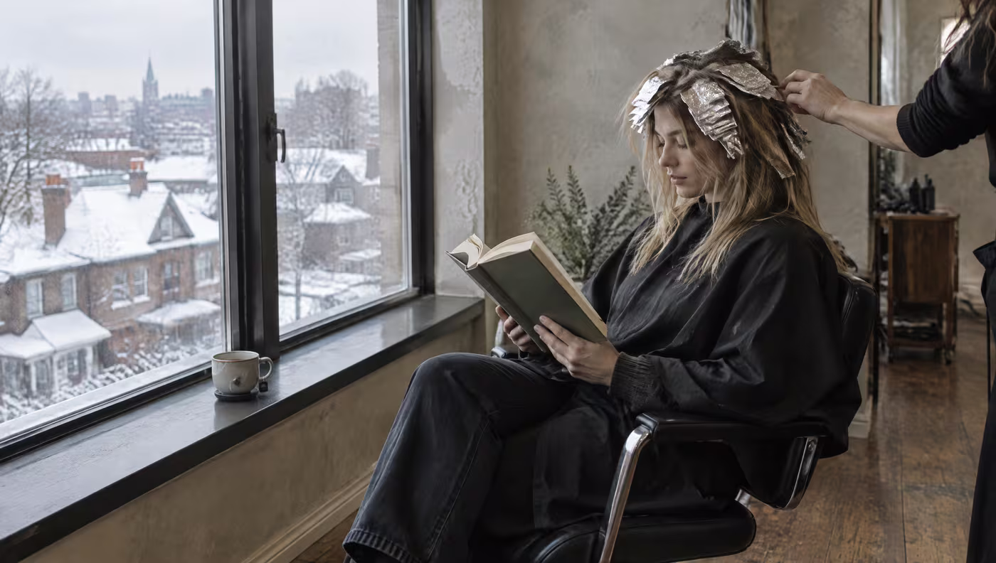A client with foils in her hair reading a book by the window with tea on the sill