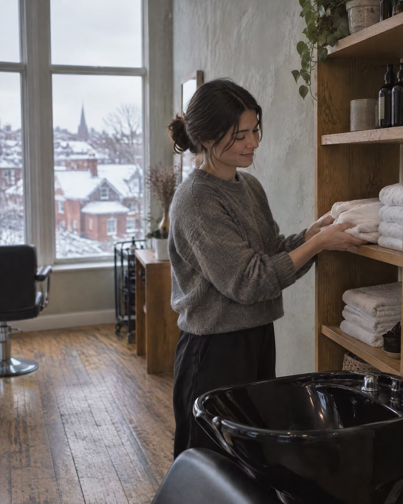 Hana folding clean towels onto an oak shelf beside the shampoo basin