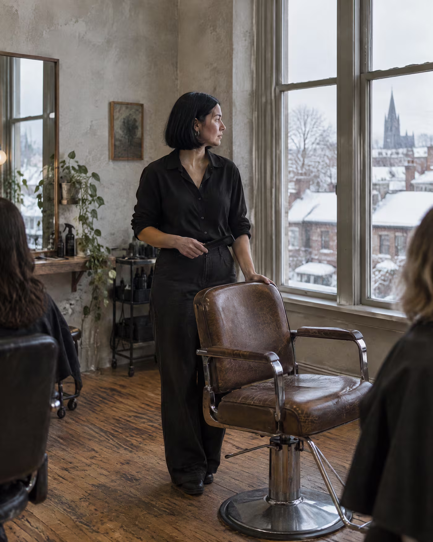 Noor standing beside an empty styling chair with a comb in her hand