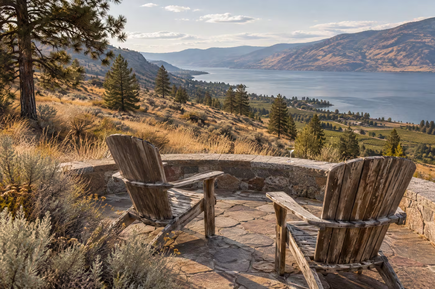 Two worn chairs on a round flagstone patio with a granite seat wall above the lake